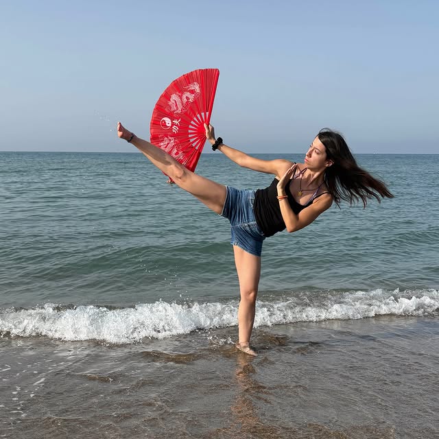 Una praticante esegue un calcio alto sulla spiaggia